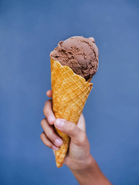 Kid hand holding chocolate ice cream cone with blue wall.