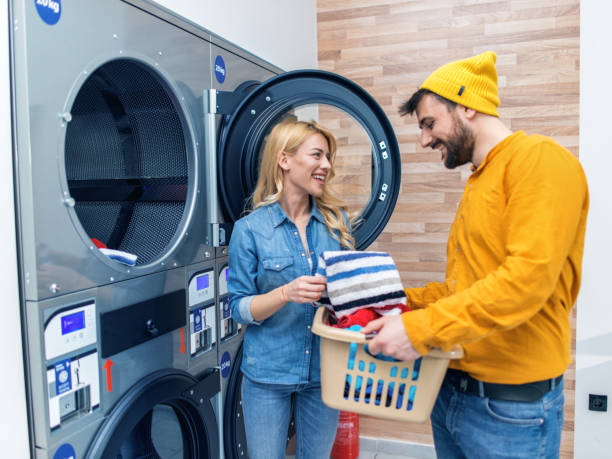 joven pareja alegre haciendo la colada juntos en la tienda de lavandería. - all laundry detergent audio fotografías e imágenes de stock