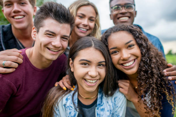 Friends Taking A Picture Together A multi-ethnic group of high school students are outdoors on a summer day. They are gathered together to take a selfie, and they are all smiling. teenager stock pictures, royalty-free photos & images