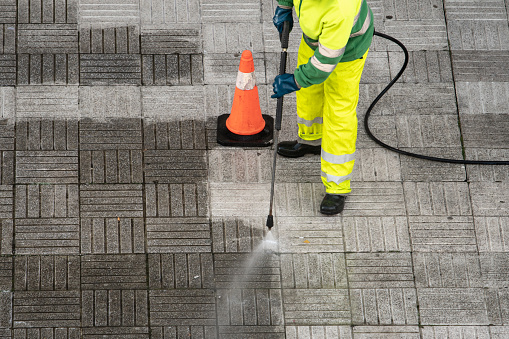 Worker cleaning the street sidewalk with high pressure water jet. Public maintenance concept