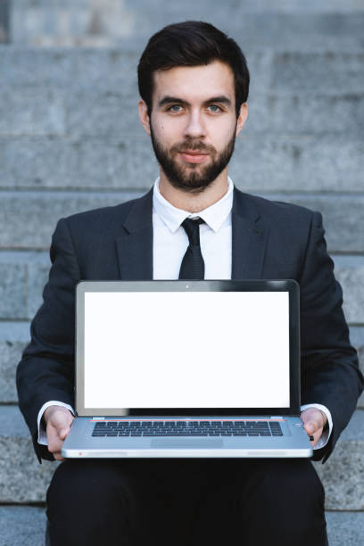 istock Outdoors businessman sitting on the steps with a laptop on his lap and looking forward. 1134309645