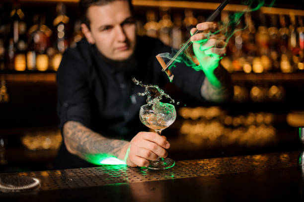 istock Bartender adding to a cocktail glass with splash and dried orange a smoked cinnamon with tweezers 1134310123