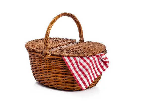 Three quarters front view of a picnic basket with a checkered tablecloth coming out of it shot on reflective white background. Useful copy space available for text and/or logo. Predominant colors are brown, red and white. High key DSRL studio photo taken with Canon EOS 5D Mk II and Canon EF 100mm f/2.8L Macro IS USM.