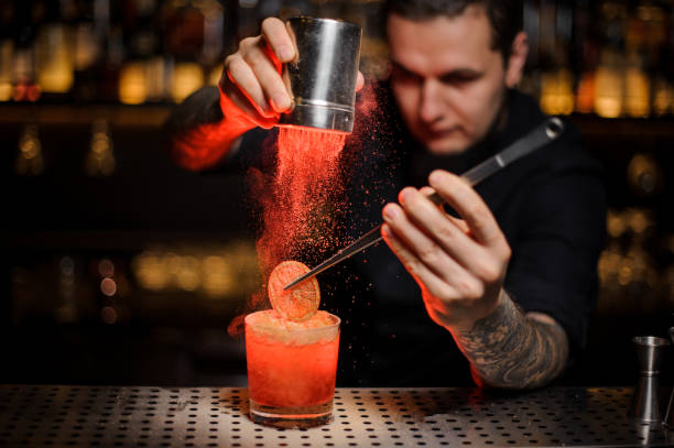 istock Professional bartender adding to an alcoholic cocktail a dried orange and powder in the red light 1134311051