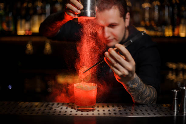 istock Professional tattooed bartender adding to an alcoholic cocktail a dried orange and powder 1134311122