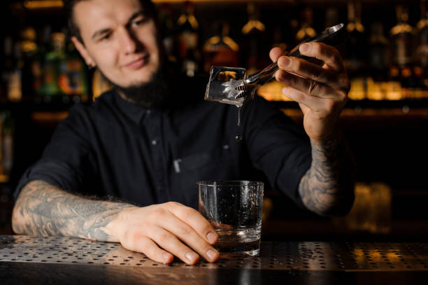 istock Smiling bartender adding to an alcoholic drink in the glass a big ice cube 1134311135