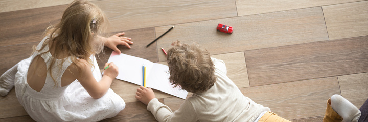 Horizontal top above photo little children preschool brother sister drawing on warm wooden floor play spend free time at modern home together, banner for website header design with copy space for text