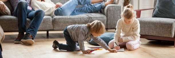 Horizontal image little kids playing drawing together on warm floor Horizontal image little kids play drawing on warm floor parents resting on couch family spend free time together, leisure activity at modern comfortable home concept, banner for website header design narrow photos stock pictures, royalty-free photos & images