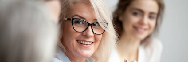 zbliżenie w wieku atrakcyjne uśmiechnięta bizneswoman słuchając kolega podczas spotkania briefingu - leadership business women senior adult zdjęcia i obrazy z banku zdjęć