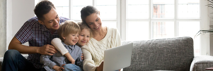 Parents little kids sitting on couch using computer watching video, family enjoy time together, buying online modern tech easy usage concept, banner for website header design with copy space for text