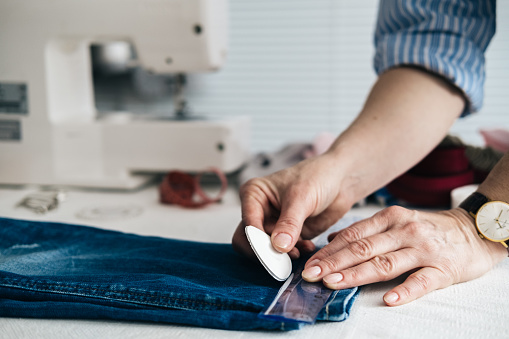 Seamstress marking hem on a pair of jeans in tailor shop