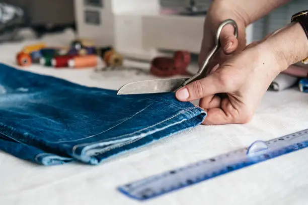 Photo of Tailor cutting jeans with scissors at workshop