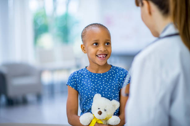Cuddling teddy A beautiful little girl smiles as she holds her teddy bear like a baby. Her doctor is facing her. She is battling cancer. cancer illness stock pictures, royalty-free photos & images