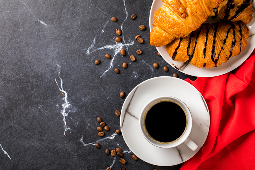 Coffee cup  with chocolate Croissant on a dark marble background with a red napkin. Black espresso.Breakfast. Top View. Flat Lay. Copy space for Text.