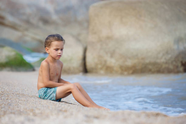 istock boy sitting on the sand by the sea 1134329857
