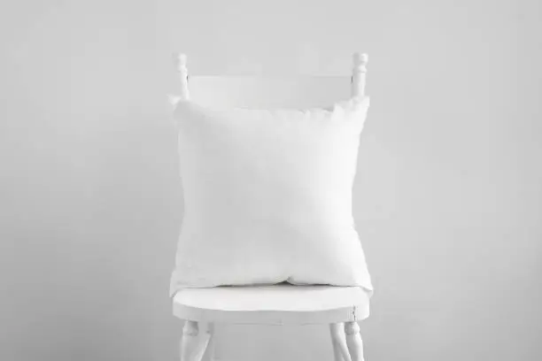 Photo of White square cushion mockup on white wooden chair.