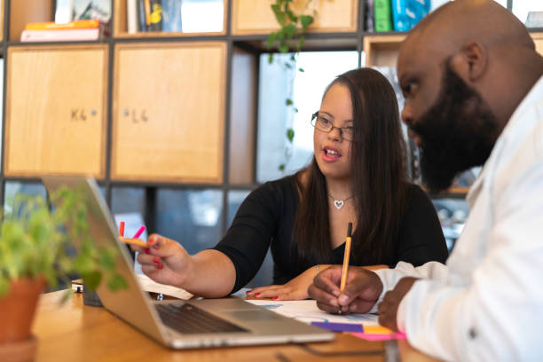 Business colleagues (including Special Needs Woman) talking about new project at modern startup office Business people working together on project in work studio down syndrome stock pictures, royalty-free photos & images