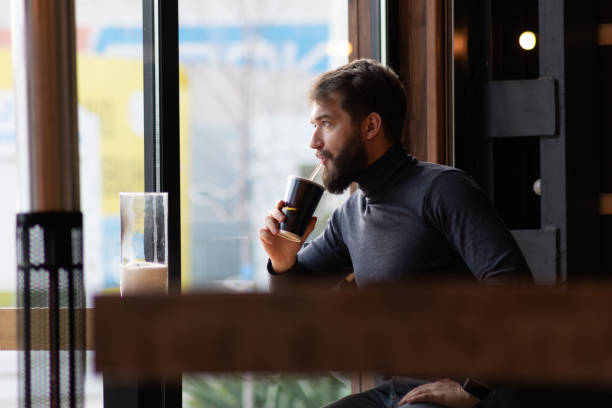 istock handsome bearded guy drinks a drink from a straw near the window in a cafe.  attractive young stylish man sitting in a cafe and looking out the window. Business, freelance 1134348006