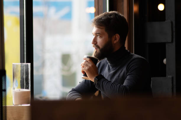 istock handsome bearded guy drinks a drink from a straw near the window in a cafe.  attractive young stylish man sitting in a cafe and looking out the window. Business, freelance 1134348036
