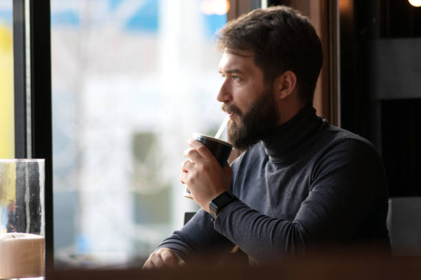 istock handsome bearded guy drinks a drink from a straw near the window in a cafe.  attractive young stylish man sitting in a cafe and looking out the window. Business, freelance 1134348110