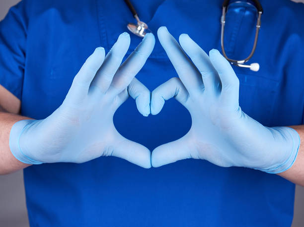 medico in uniforme blu e vecchi guanti di lattice che mostrano gesto del cuore - nurse paramedic healthcare and medicine hygiene foto e immagini stock