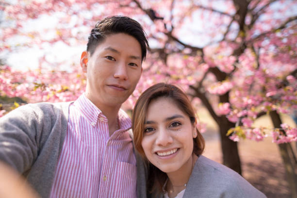 Multi-ethnic couple taking selfie picture in front of cherry blossoms