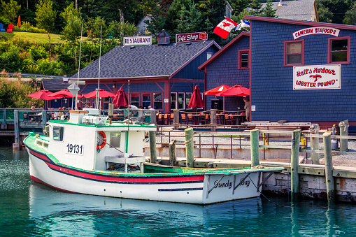 Hall's Harbour, Nova Scotia, Canada - August 29, 2015: The boat Frenchy Bay is docked near Hall's Harbour Lobster Pound during high tide. In the background people are enjoying a meal at the restaurant.