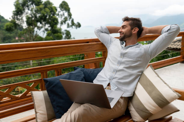 Relaxed man working online at home on the balcony using a laptop computer