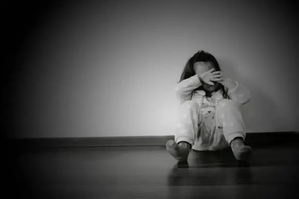 Photo of 3 year old little girl closed her face sitting on the floor in front of the wall in black and white backdrop