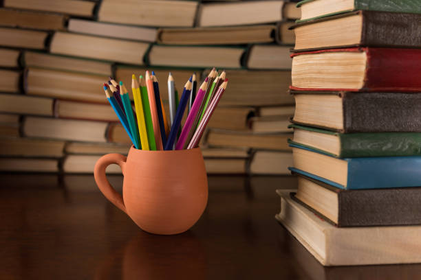 colored pencils in a mug on the background of books