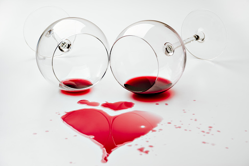 Red wine spilled from two turned wineglasses making a heart shape over a white table