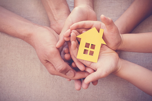 Adult and child hands holding yellow house, family home and homeless shelter concept