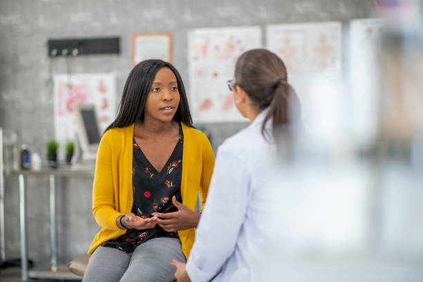 Patient Describing Symptoms A woman of African descent and her doctor are indoors in a medical clinic. The woman is sitting and describing her symptoms to the doctor. symptom photos stock pictures, royalty-free photos & images