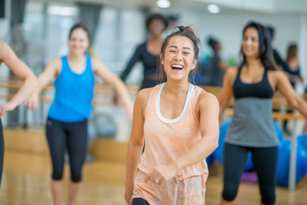 Dance Class A multi-ethnic group of adult women are dancing in a fitness studio. They are wearing athletic clothes. An Asian woman is in front, and she is smiling at the camera while dancing. zumba image stock pictures, royalty-free photos & images
