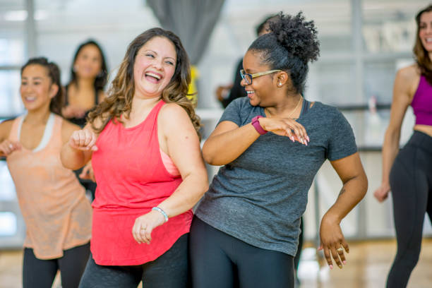 Women Dancing Together A multi-ethnic group of adult women are dancing in a fitness studio. They are wearing athletic clothes. Two women are laughing while dancing together. 45 49 years photos stock pictures, royalty-free photos & images