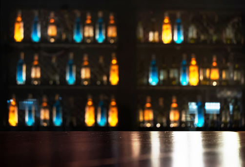 top of wood table with neon orange blue light of glass alcohol bottle in dark bar and club background