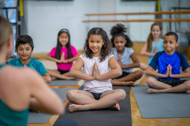 Class Meditation A teacher is leading her students during physical education class. She is meditating with her hands together, and her students are following her. They are all wearing casual athletic clothing. mindfulness children stock pictures, royalty-free photos & images