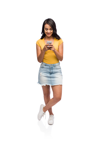 Full body shot of latin woman texting on her phone with one leg crossed over the other.