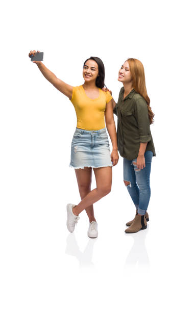 Two young women taking a selfie Two beautiful young women taking a selfie together wearing casual clothing isolated on a white background. full body isolated stock pictures, royalty-free photos & images