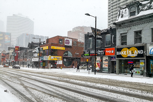 Toronto, Canada - February 27, 2019: People walking in the snow on Yonge Street looking South from Gerrard St E in Toronto Canada.