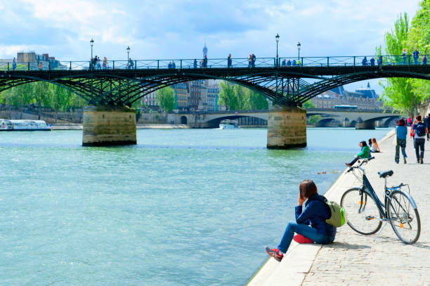 Paris, France - April 25, 2018: Young woman resting with a bicycle on the quay along the Seine River in Paris