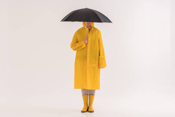 mittelerwachsene frau in gelbem regenmantel und regenstiefel - regenmantel stock-fotos und bilder
