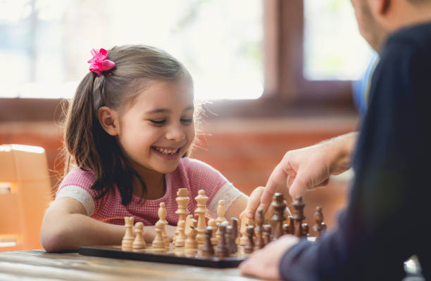 padre enseñando a su hija a jugar al ajedrez en casa - juego de ajedrez fotografías e imágenes de stock