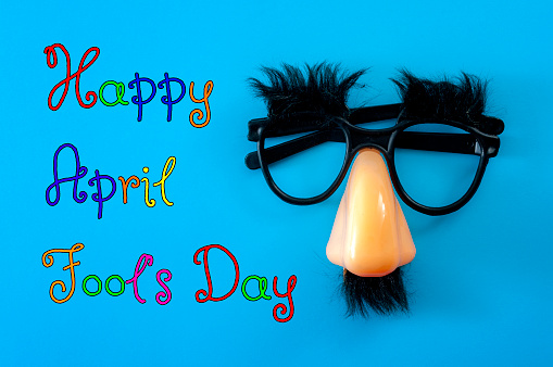 Happy april fool's day and funny pranks concept with a pair of comical glasses with bushy eyebrows and thick mustache isolated on blue background