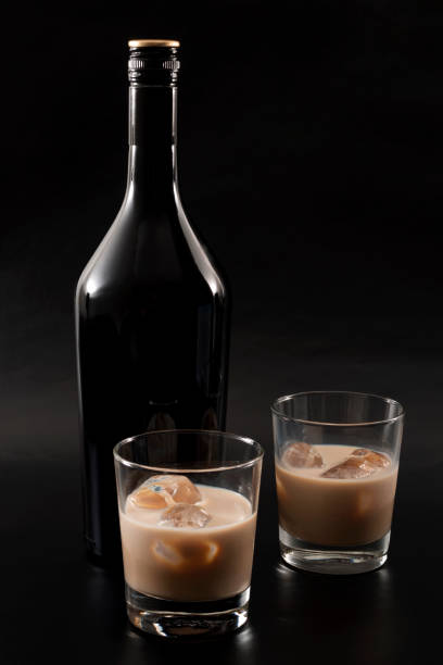 Coffee liqueur and alcoholic beverages based on milk and whiskey concept with Irish cream bottle and glasses with ice isolated on dark black background