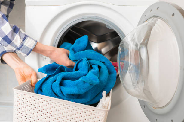 persons hand put dirty clothes in the washing machine b stock photo