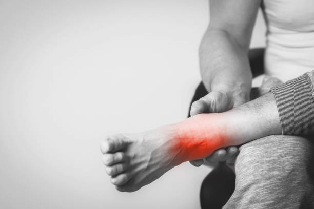 man with pain in foot Causian man holds hands to his painful feet, pain in foot.  Black and white photography. red color is area of pain ankle photos stock pictures, royalty-free photos & images