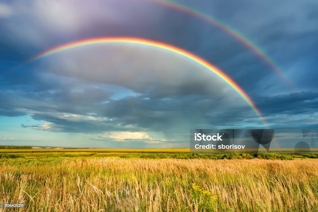 Rainbow over stormy sky in countryside at summer day Rainbow over stormy sky. Rural landscape with rainbow over dark stormy sky in a countryside at summer day. Rainbow Stock Photo