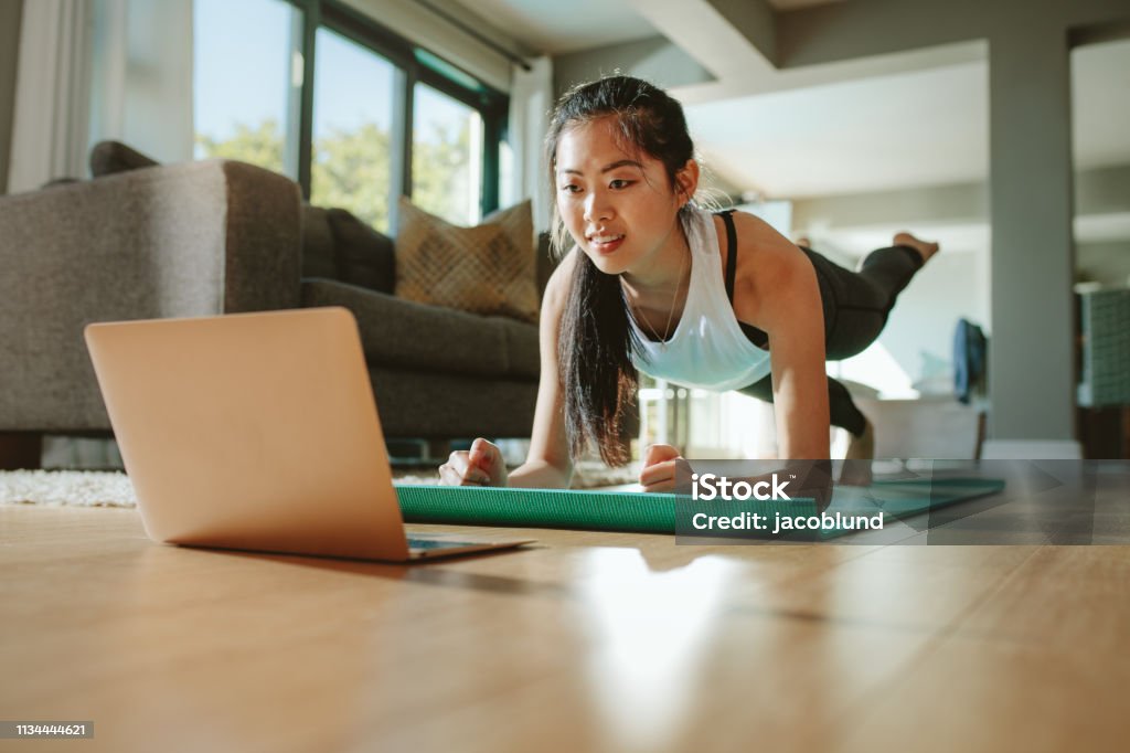 Woman watching sport training online on tablet Woman working out at home watching video tutorial on laptop. Fit young woman in plank position repeating online instructions by coach on computer. Exercising Stock Photo