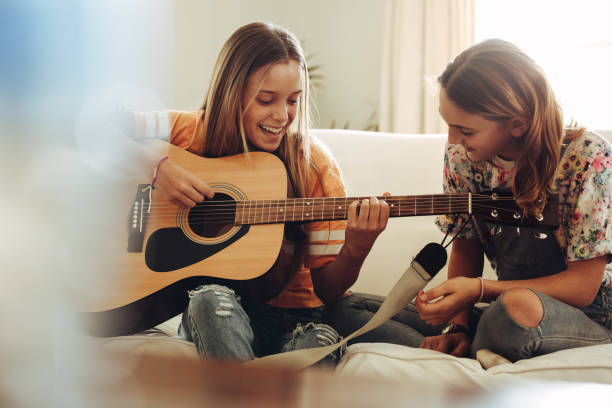 chicas divirtiéndose aprendiendo guitarra - plucking an instrument fotografías e imágenes de stock